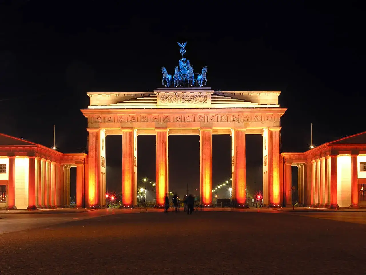 Das Brandenburger Tor erstrahlt nachts in warmem Licht. Die Quadriga thront &uuml;ber den S&auml;ulen.