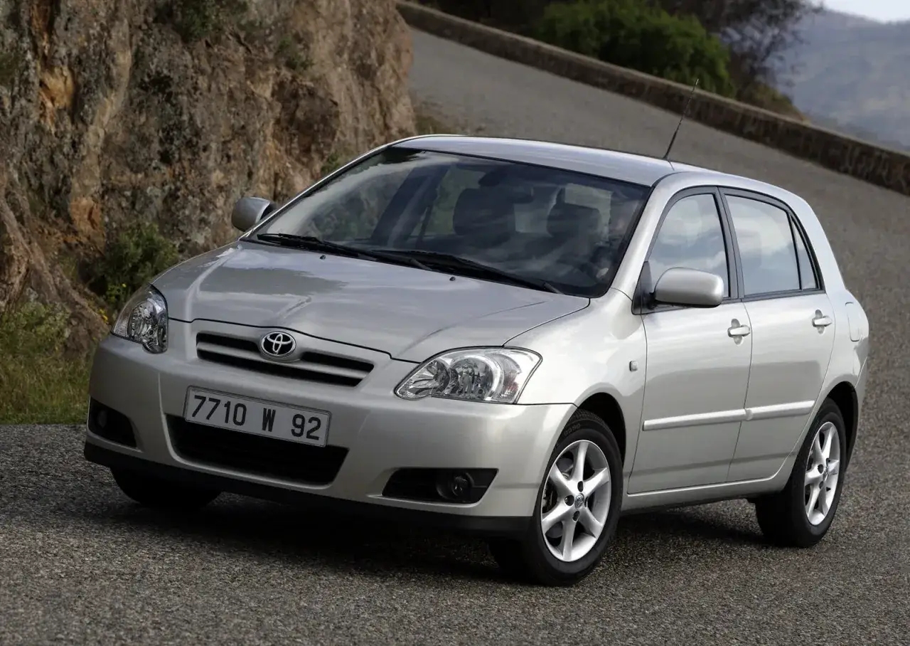 Srebrna Toyota Corolla E12 hatchback na krętej drodze, z kamienistym zboczem w tle.