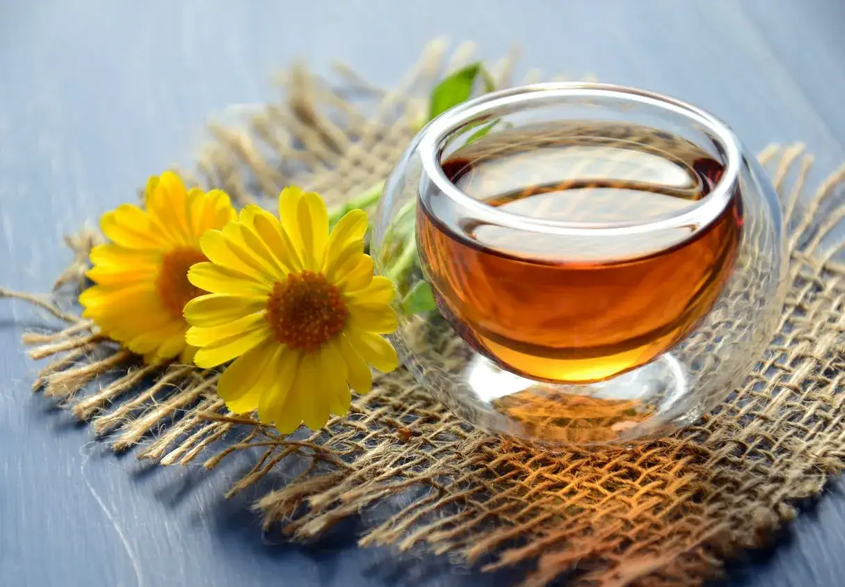 Une tasse de tisane pour dig&eacute;rer le soir, accompagn&eacute;e de deux fleurs jaunes sur un tissu de jute.
