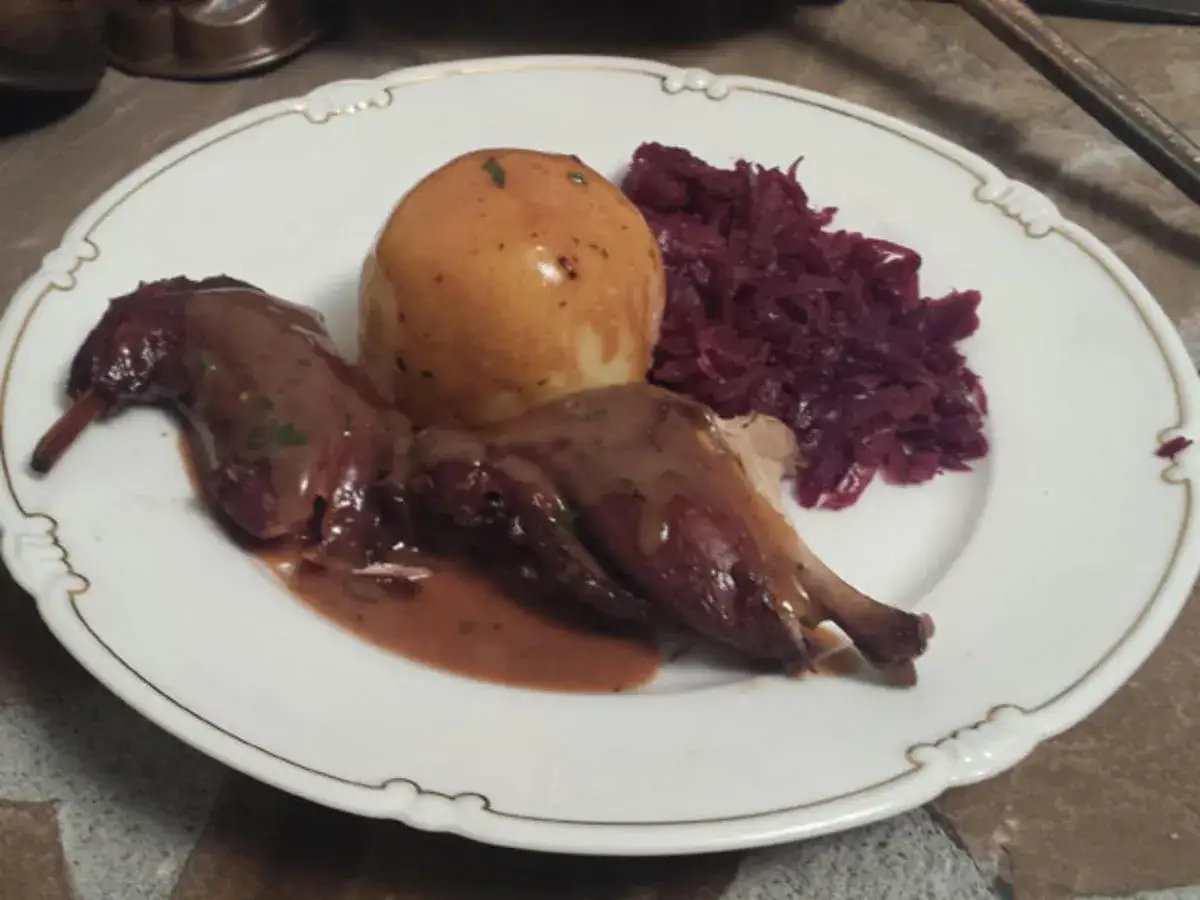 Zwei Kaninchenbraten in dunkler Sauce, serviert mit Kl&ouml;&szlig;en und Rotkohl auf einem Teller.