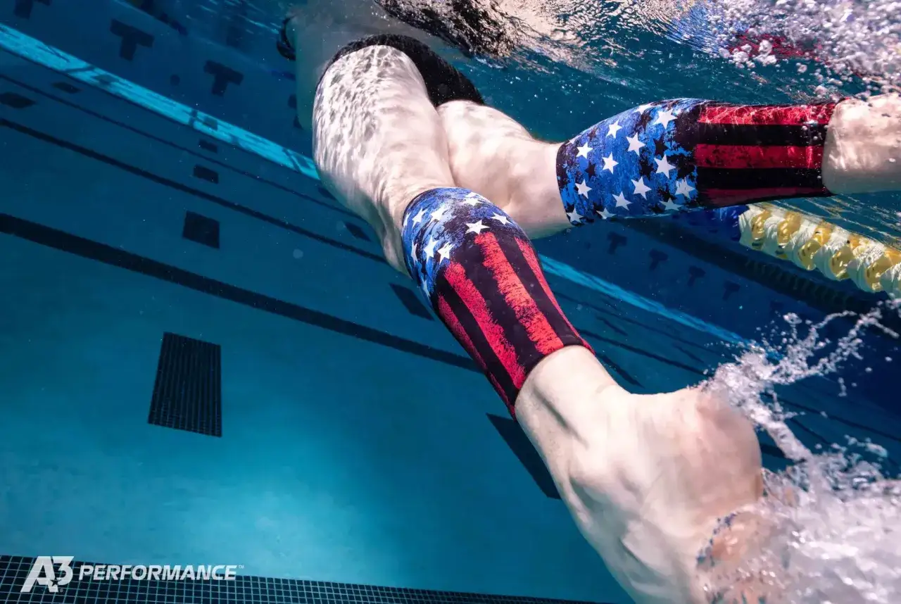 Underwater view of a swimmer's legs in a pool, wearing patriotic swim trunks. Ever wonder why do I get foot cramps in the pool?