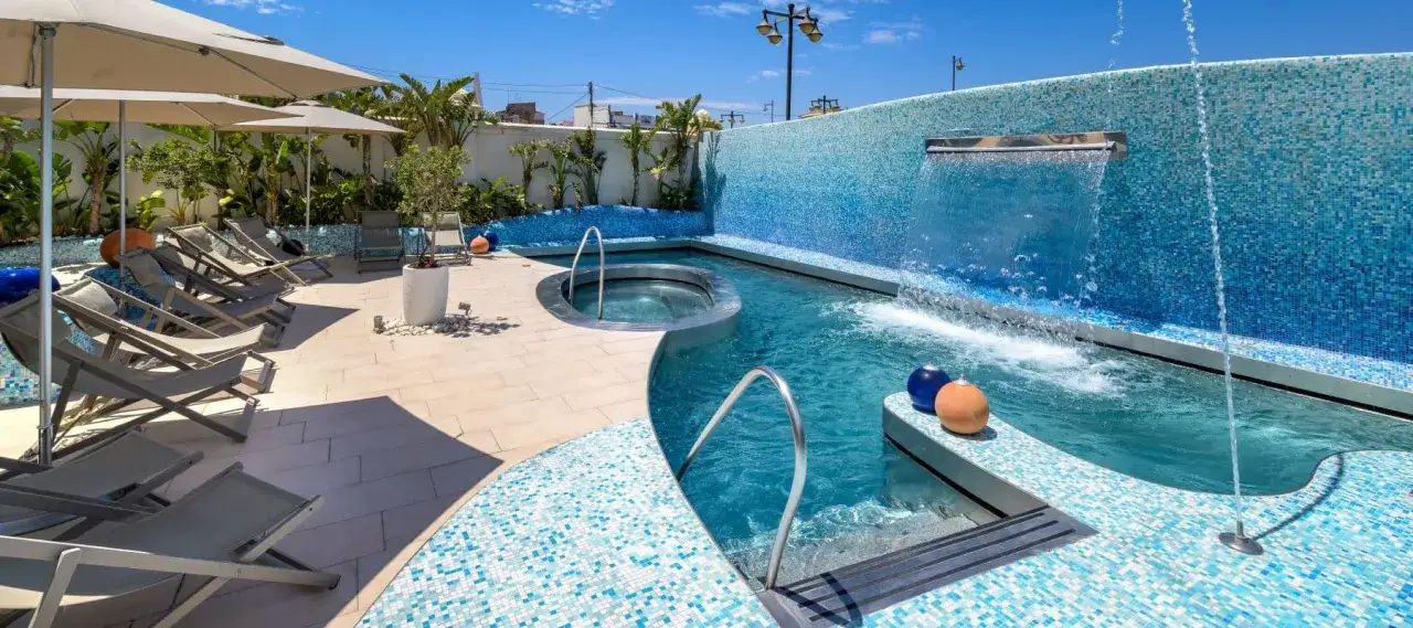 Relájate en este spa en Valencia con piscina, jacuzzi y cascada. Tumbonas y sombrillas invitan al descanso bajo el sol.