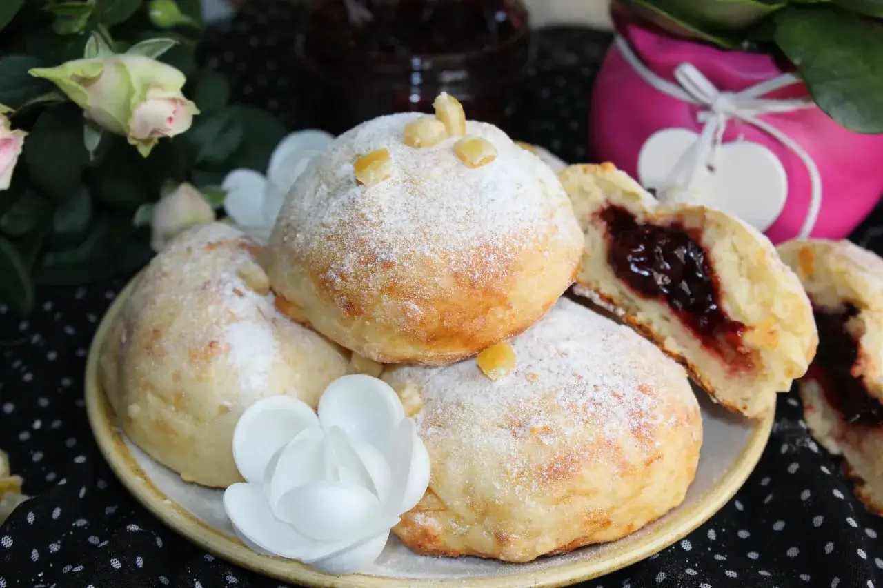 Puszyste pączki z dżemem, posypane cukrem pudrem, wyglądają jak fit przekąska na talerzu.