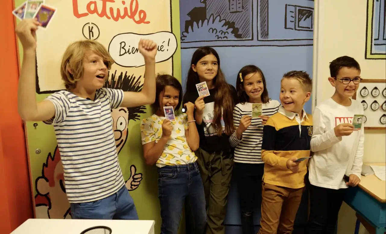 Des enfants heureux participent &agrave; un escape game, tenant des cartes color&eacute;es. L'un d'eux l&egrave;ve les bras en signe de victoire.