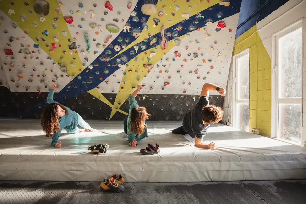 Drei junge Leute &uuml;ben das, was ist bouldern: Klettern an einer Wand ohne Seil, nur mit dicken Matten darunter.