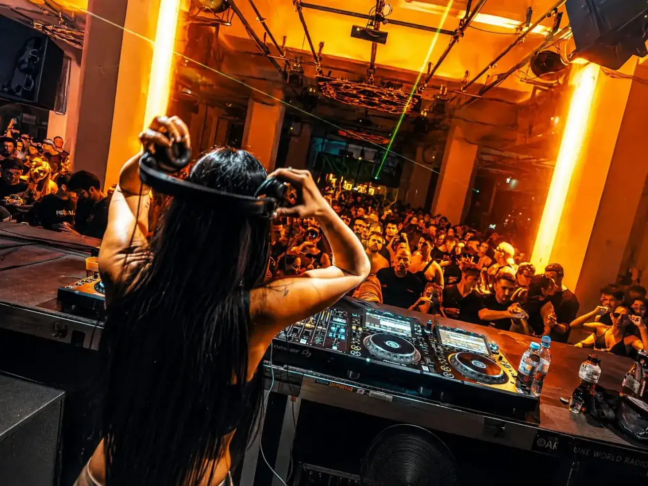 DJ con cuffie, folla in delirio e luci arancioni creano l'atmosfera perfetta per la musica house famosa.