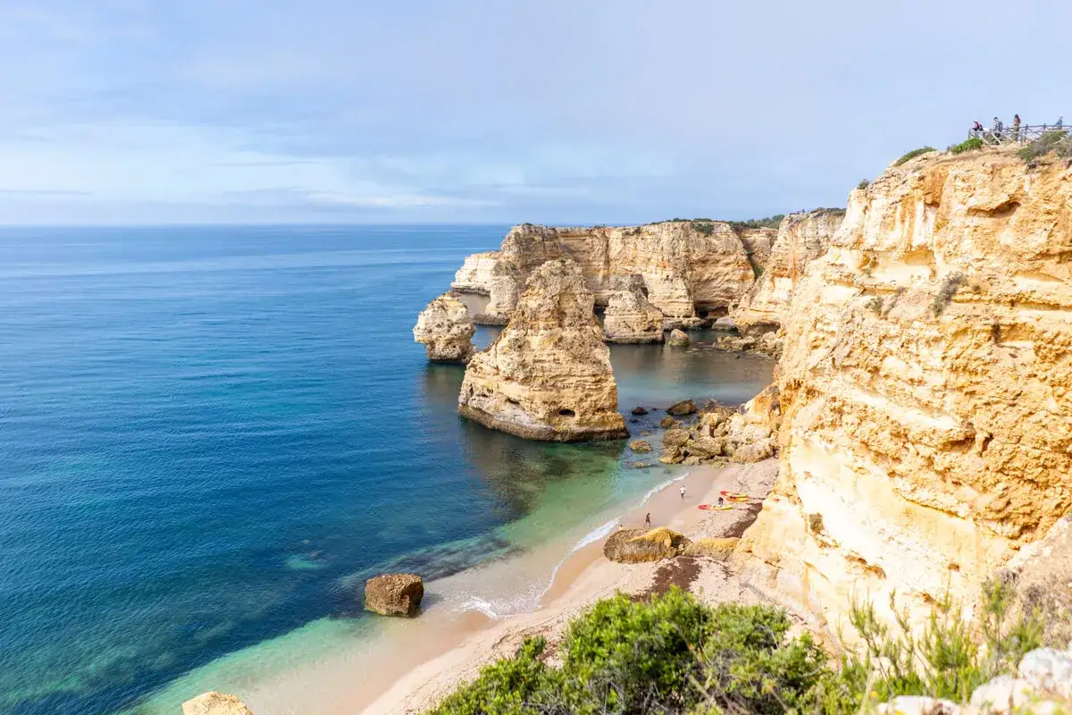 Atemberaubende Felsformationen am Praia da Marinha, Algarve. Türkisfarbenes Wasser trifft auf goldene Klippen, kleine Boote und Menschen am Strand.