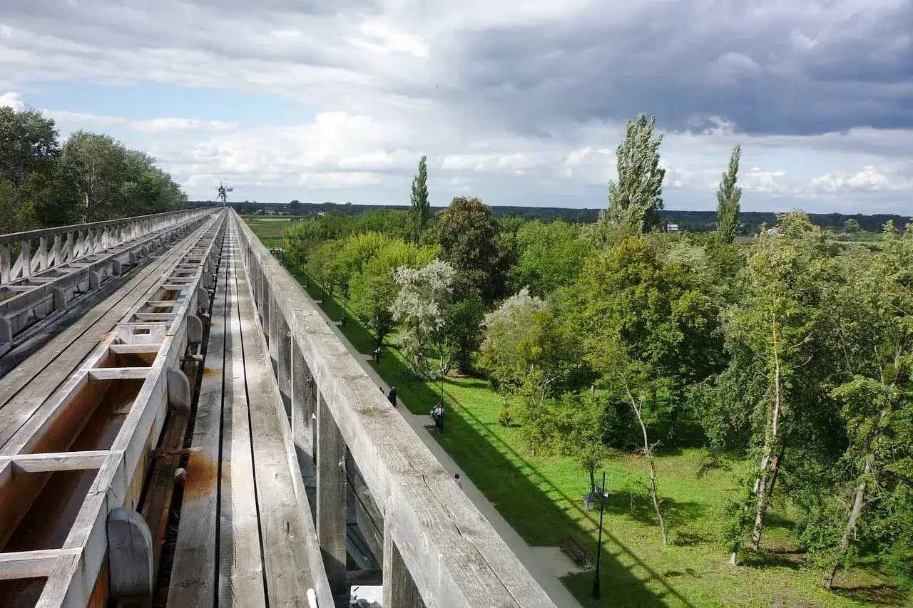 Drewniany most nad zielonym parkiem, idealne miejsce na zwiedzanie okolic Ciechocinka. W oddali widać wiatrak.