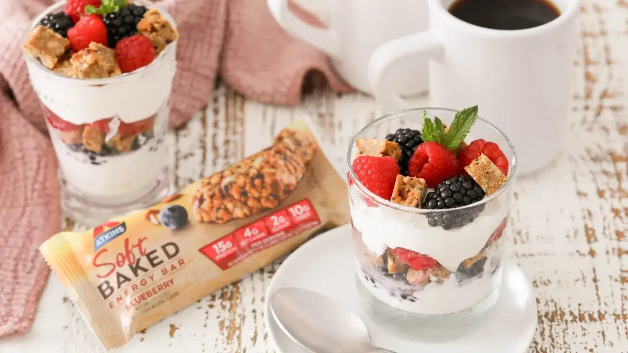 Ein Glas mit Joghurt, Beeren und Keksstückchen. Daneben eine Riegelpackung, die für low carb joghurt steht.