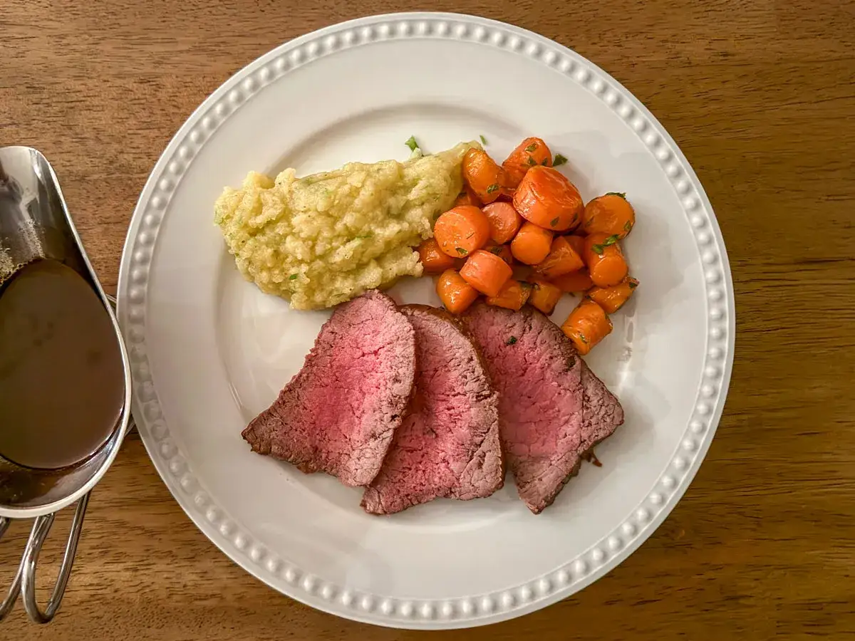 Tranch&eacute; de rosbif saignant, pur&eacute;e de pommes de terre et carottes glac&eacute;es, servi avec une sauce au vin rouge.