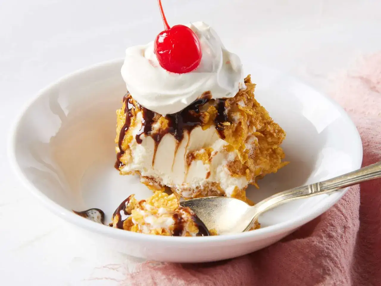 Ein St&uuml;ck gebratenes Eis mit Schokoladensauce, Sahne und Kirsche in einer wei&szlig;en Sch&uuml;ssel.