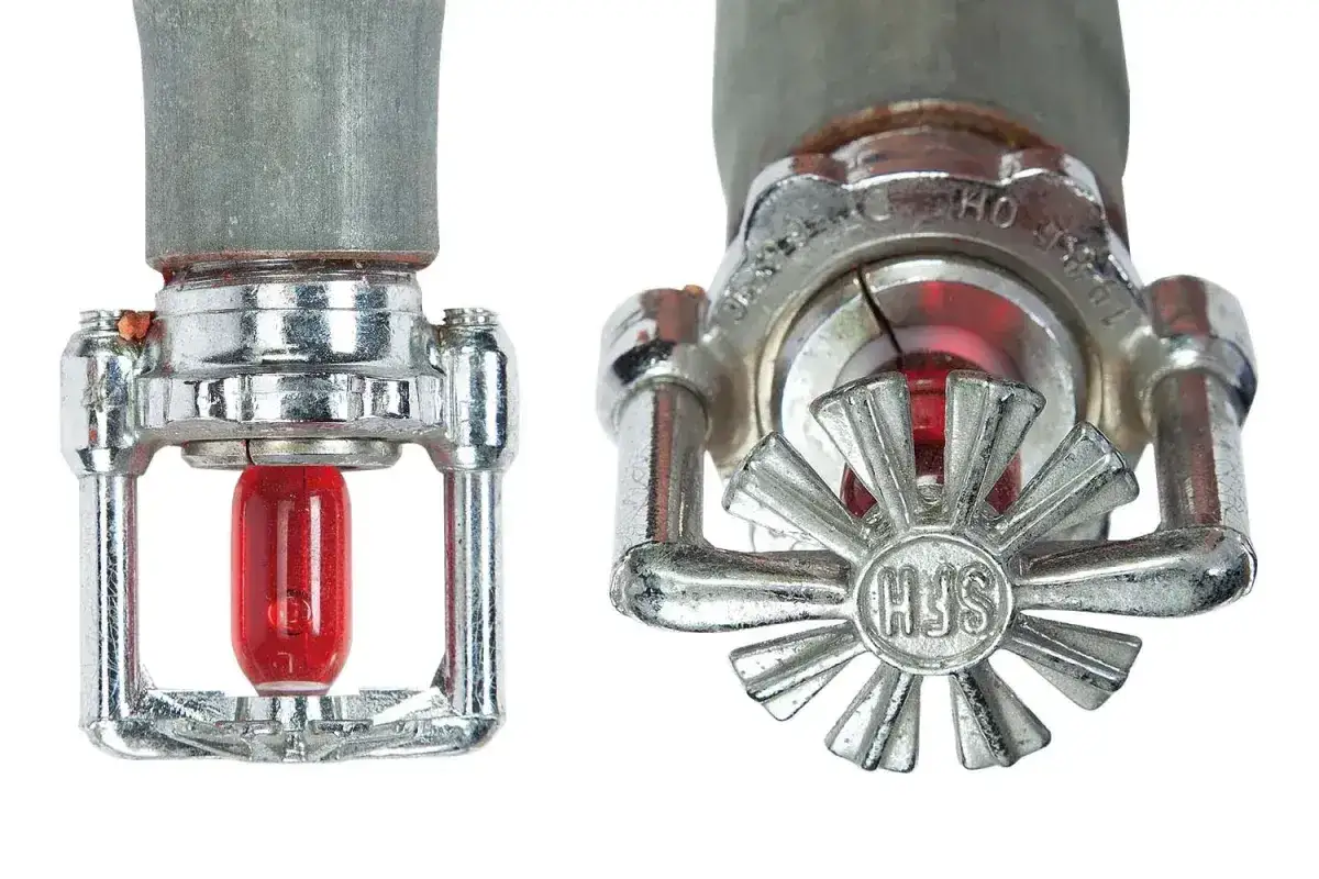 Zwei Sprinklerköpfe für die Wartung von Sprinkleranlagen, einer mit sichtbarem roten Glasfässchen, der andere mit einem Stern-Deflektor.
