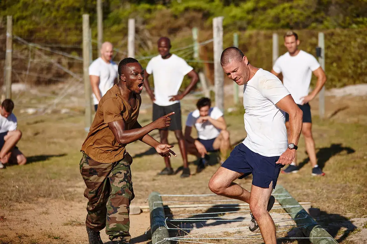 Intensywny trening wojskowy. Dw&oacute;ch mężczyzn w akcji, jeden wskazuje, drugi pokonuje przeszkodę.
