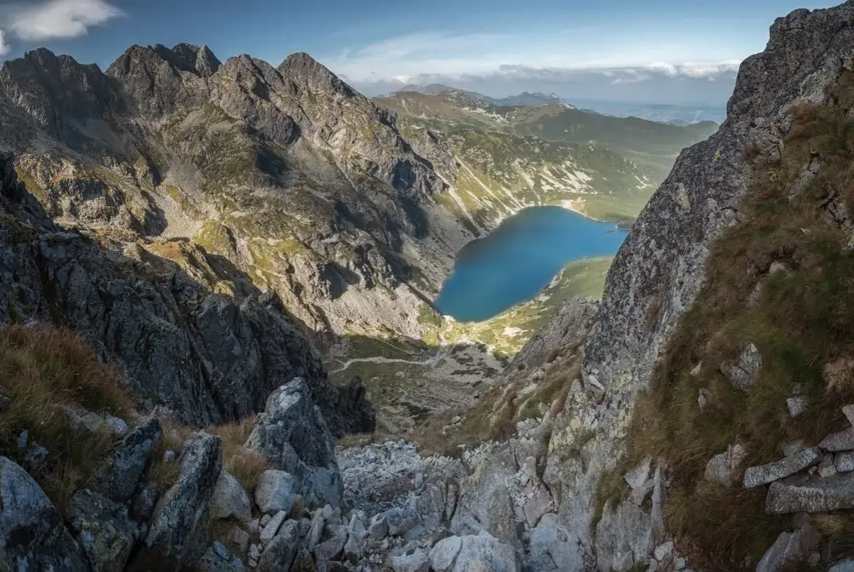 Widok z Orlej Perci na Morskie Oko. Kamienista ścieżka wije się wśród skalistych zboczy, prowadząc do turkusowego jeziora.