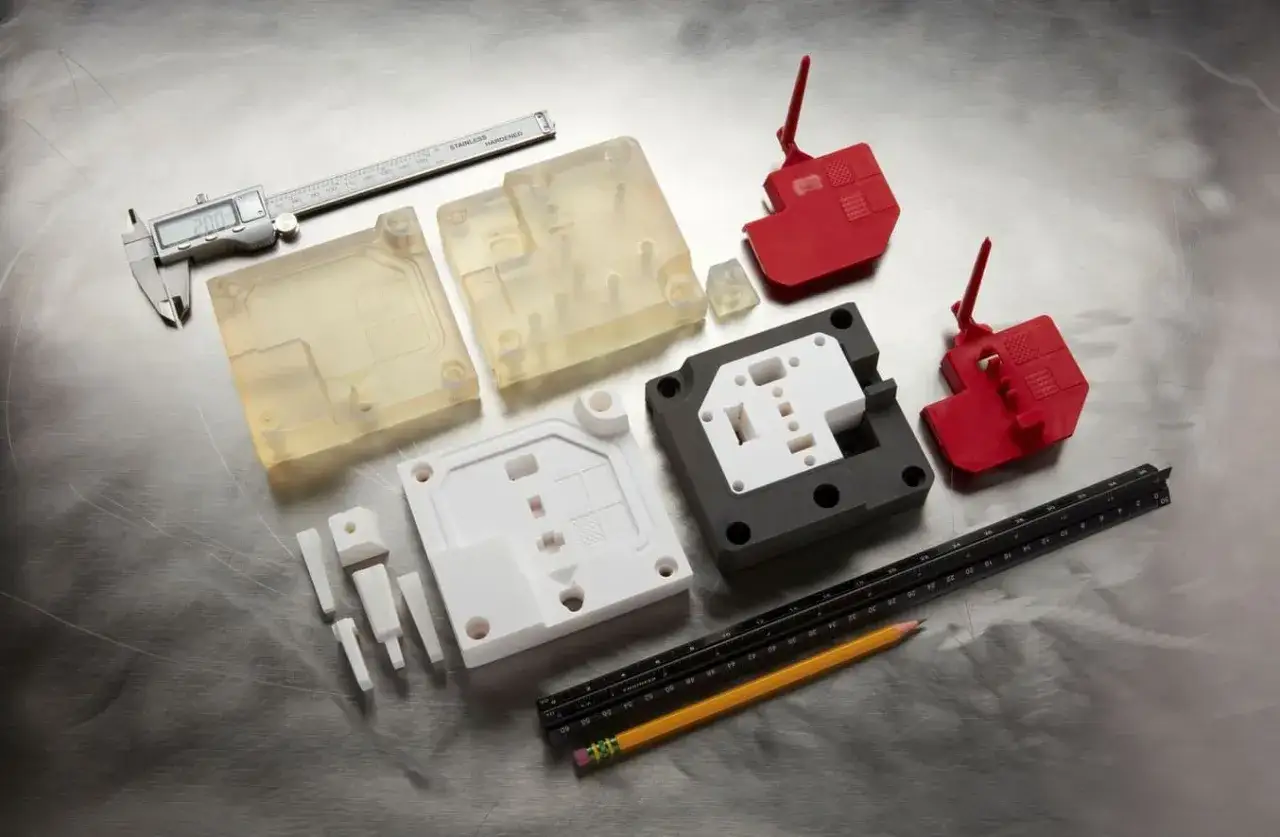 Various 3d printed molds in different colors and materials, alongside a caliper, ruler, and pencil, suggest precision engineering and prototyping.