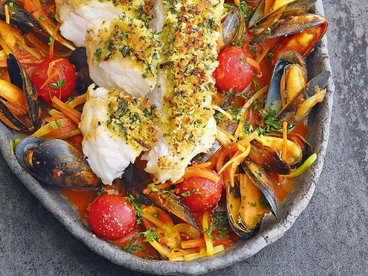 Seeteufel im Wasser, serviert mit Muscheln, Tomaten und Gem&uuml;se in einer w&uuml;rzigen Sauce.