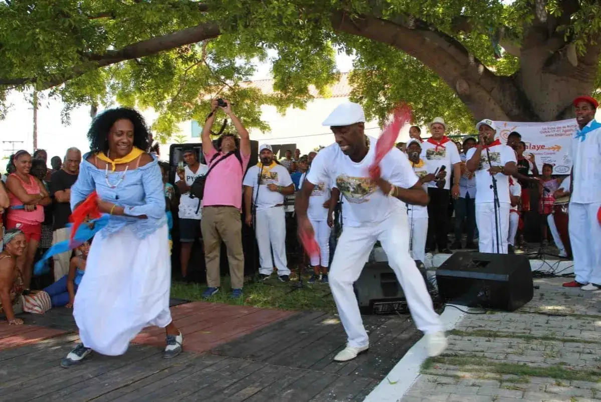 Pareja baila rumba cubana con pa&ntilde;uelos. M&uacute;sicos y p&uacute;blico observan. Diversos tipos de rumba se celebran.