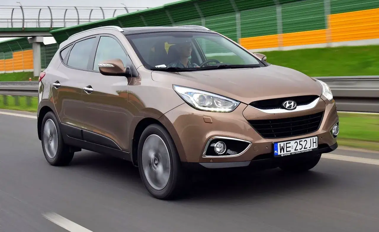 Brązowy Hyundai ix35 w ruchu drogowym, z widocznym kierowcą i tablicą rejestracyjną WE 252 JH.