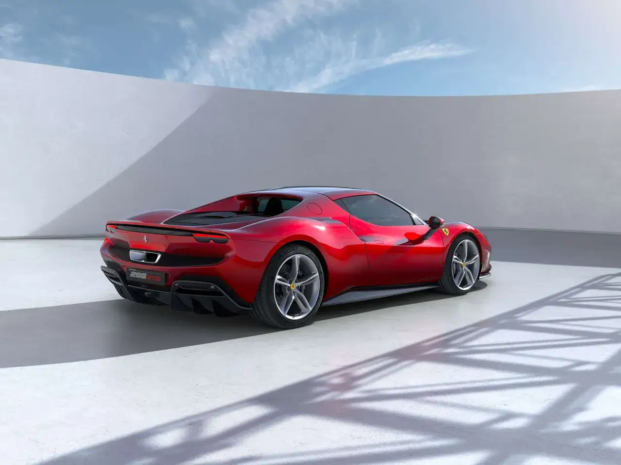 Czerwone Ferrari 296 GTB z ostrymi liniami i sportowym dyfuzorem, stojące na tle białej ściany i błękitnego nieba.