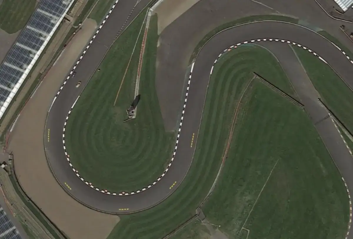 Vista aérea de una curva en S de un circuito de carreras, con una moto de MotoGP preparándose para un long lap.