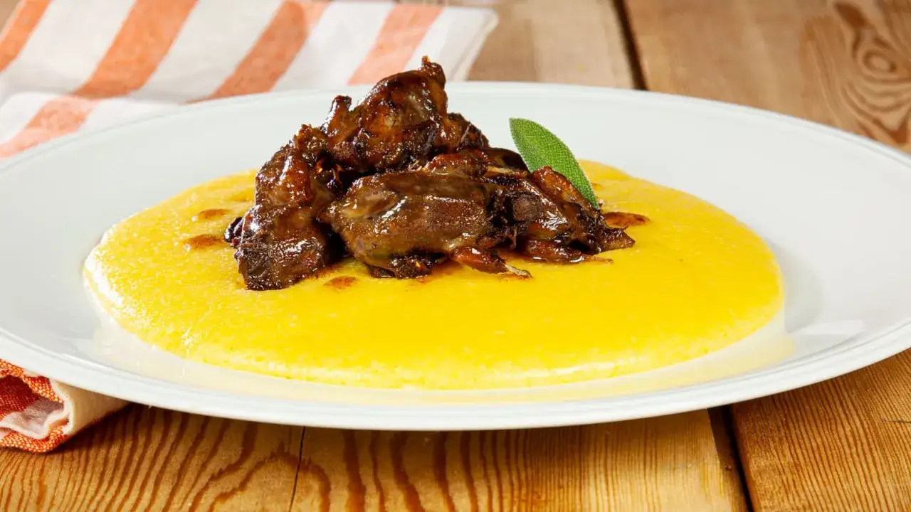 Piatto di polenta e osei, con uccellini scuri e succulenti adagiati sulla morbida polenta gialla, guarnito con una foglia di salvia.