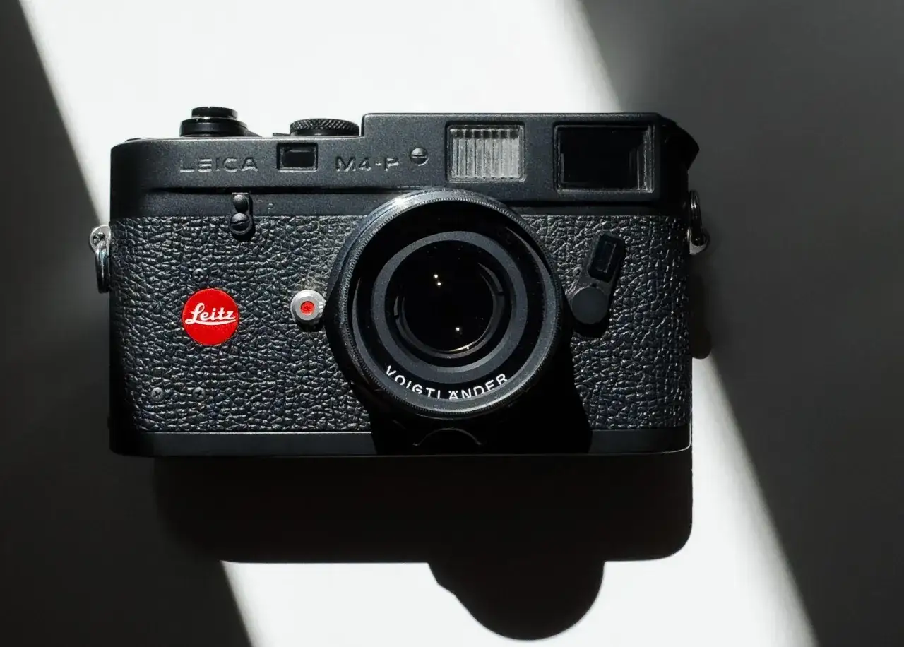 A black Leica M4-P camera with a Voigtlander lens sits on a white surface, casting a dramatic shadow.
