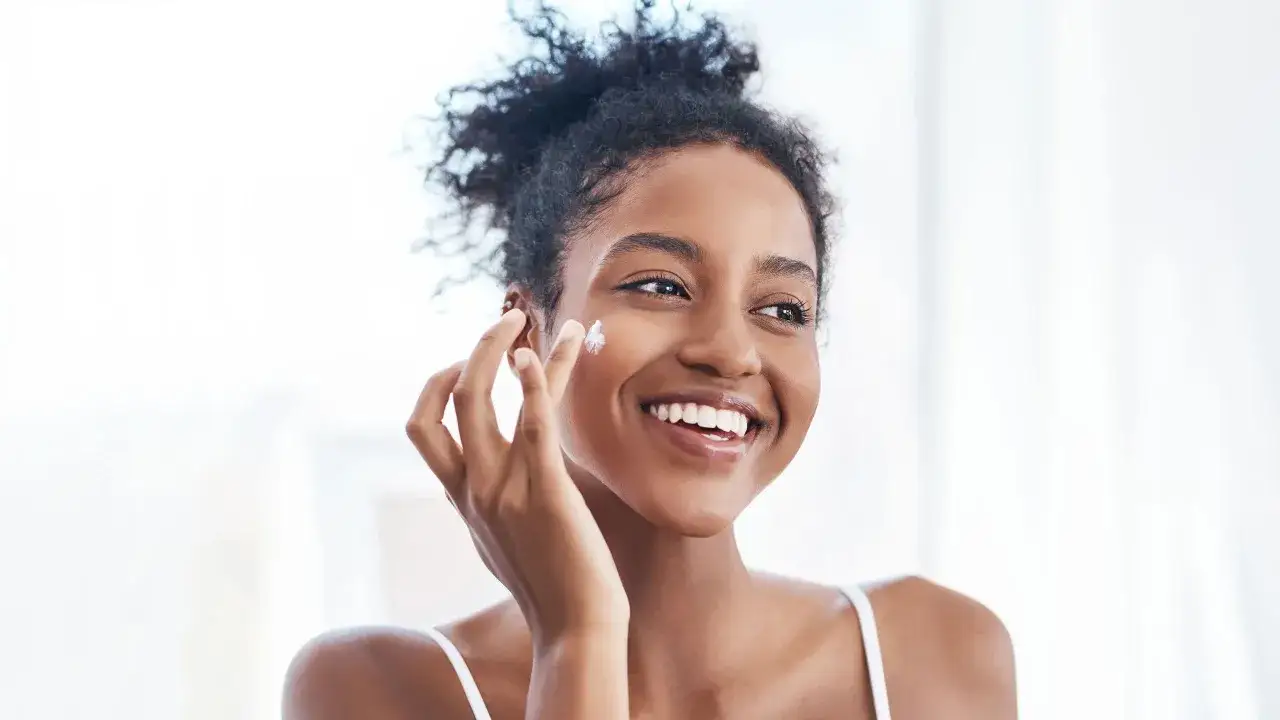 Une femme applique une cr&egrave;me sur sa joue, se demandant si c'est une cr&egrave;me solaire avant ou apr&egrave;s la cr&egrave;me hydratante.
