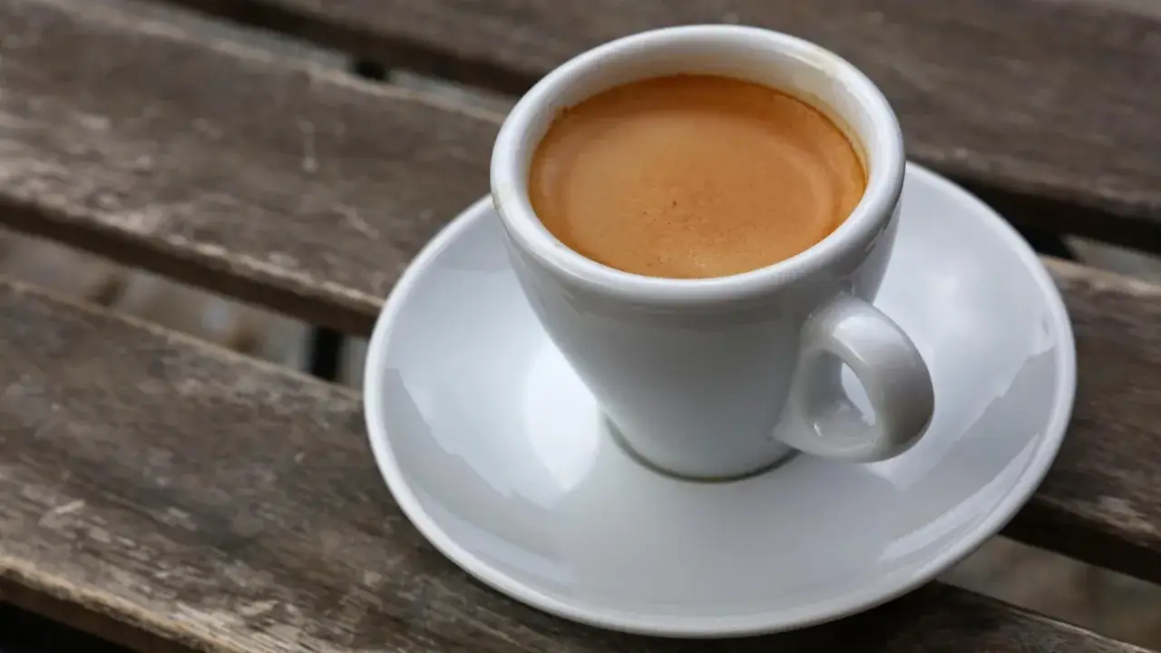 Mała filiżanka kawy espresso z pianką na drewnianym blacie. Espresso co to? Intensywny nap&oacute;j kawowy.