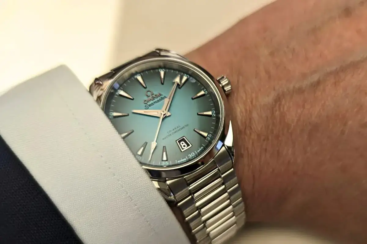 Un elegante Omega Seamaster con quadrante azzurro e indici luminosi, indossato su un polso con camicia bianca.