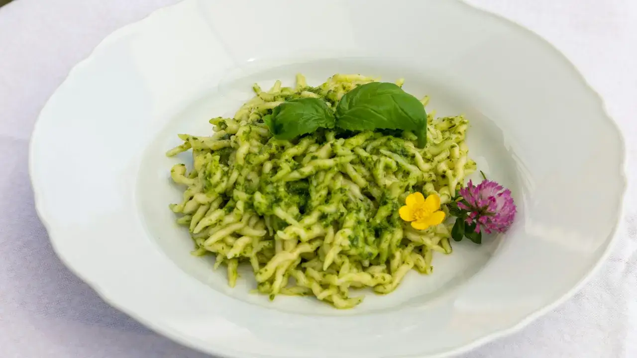 Pâtes au pesto, une recette italienne simple et savoureuse, garnie de basilic frais et de fleurs comestibles.