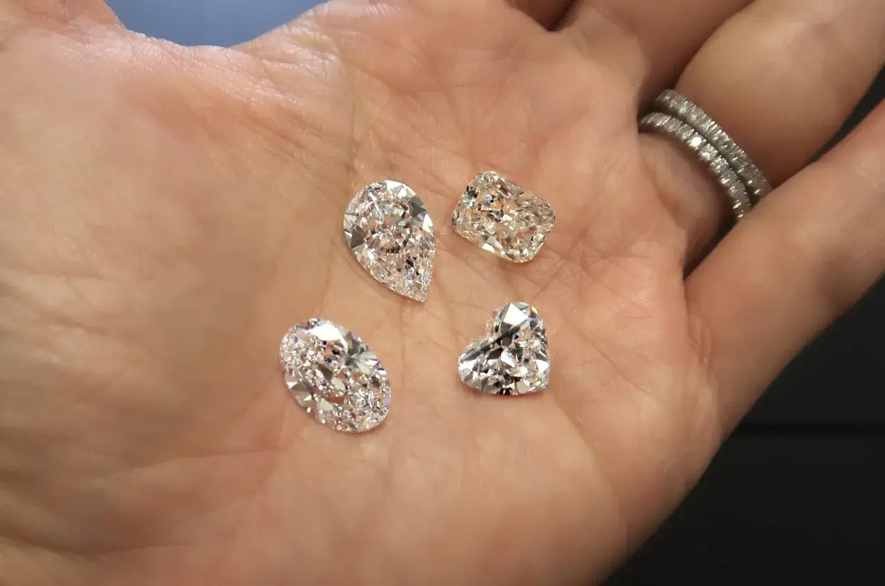 Four sparkling, faceted gemstones are held in a palm. These are not natural diamonds, but rather what does simulated diamond mean? They are lab-created stones mimicking diamond's brilliance.