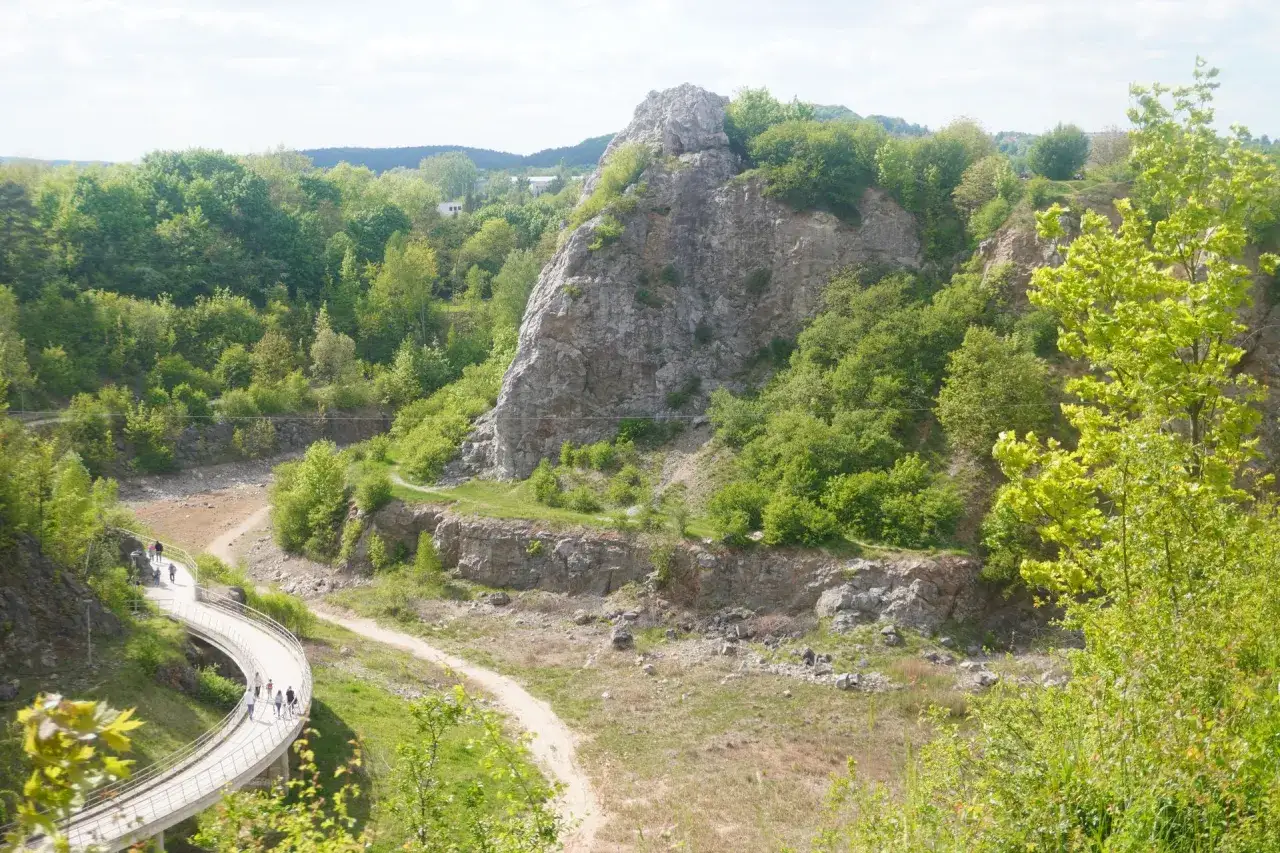 Kamieniołom w Kielcach z krętą ścieżką i grupą spacerowicz&oacute;w. W oddali skaliste g&oacute;ry porośnięte zielenią.