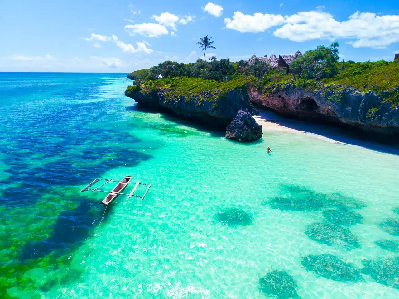 Un paradis tropical en Tanzanie, idéal pour savoir quand partir en Tanzanie. Eau turquoise, pirogue, et une personne nageant près d'une plage isolée.