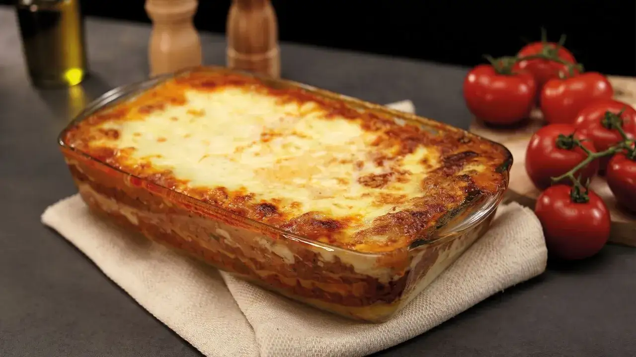 Ein frisch gebackenes Lasagne Rezept original italienisch in einer Glasform, daneben frische Tomaten.