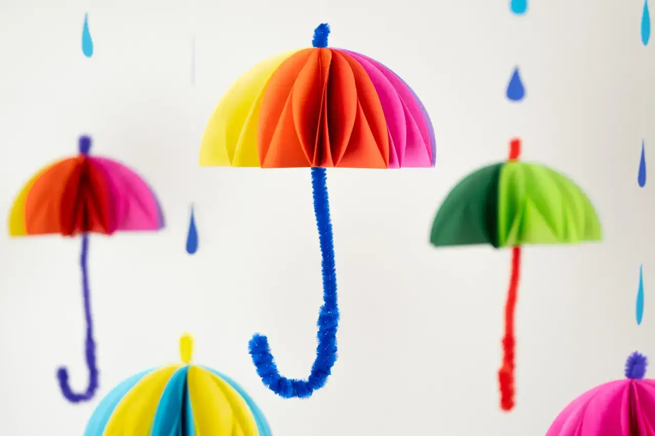 Bunte Papier-Regenschirme hängen von der Decke. Ein einfaches Bastelprojekt für Kinder, das gute Laune macht.