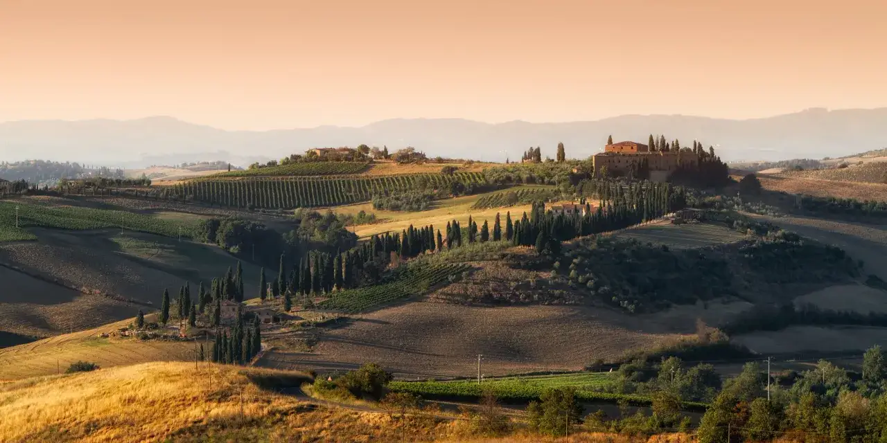 Sanfte H&uuml;gel im Val d'Orcia, ges&auml;umt von Zypressen und Weinbergen, mit einer Villa im Abendlicht.