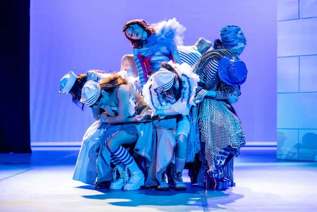 Grupa aktorów w marynistycznych strojach na scenie. Teatr Gdynia spektakle w błękitnym świetle.