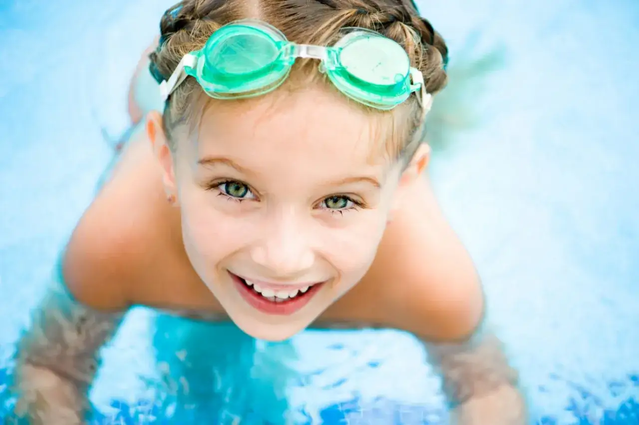Niña sonriente con gafas de natación en la piscina, disfrutando de las actividades de verano.