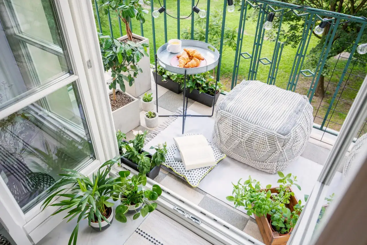 Acogedor balc&oacute;n con plantas, cojines, un puf y un caf&eacute; con cruasanes. Un rinc&oacute;n perfecto para disfrutar de terrazas peque&ntilde;as con encanto.