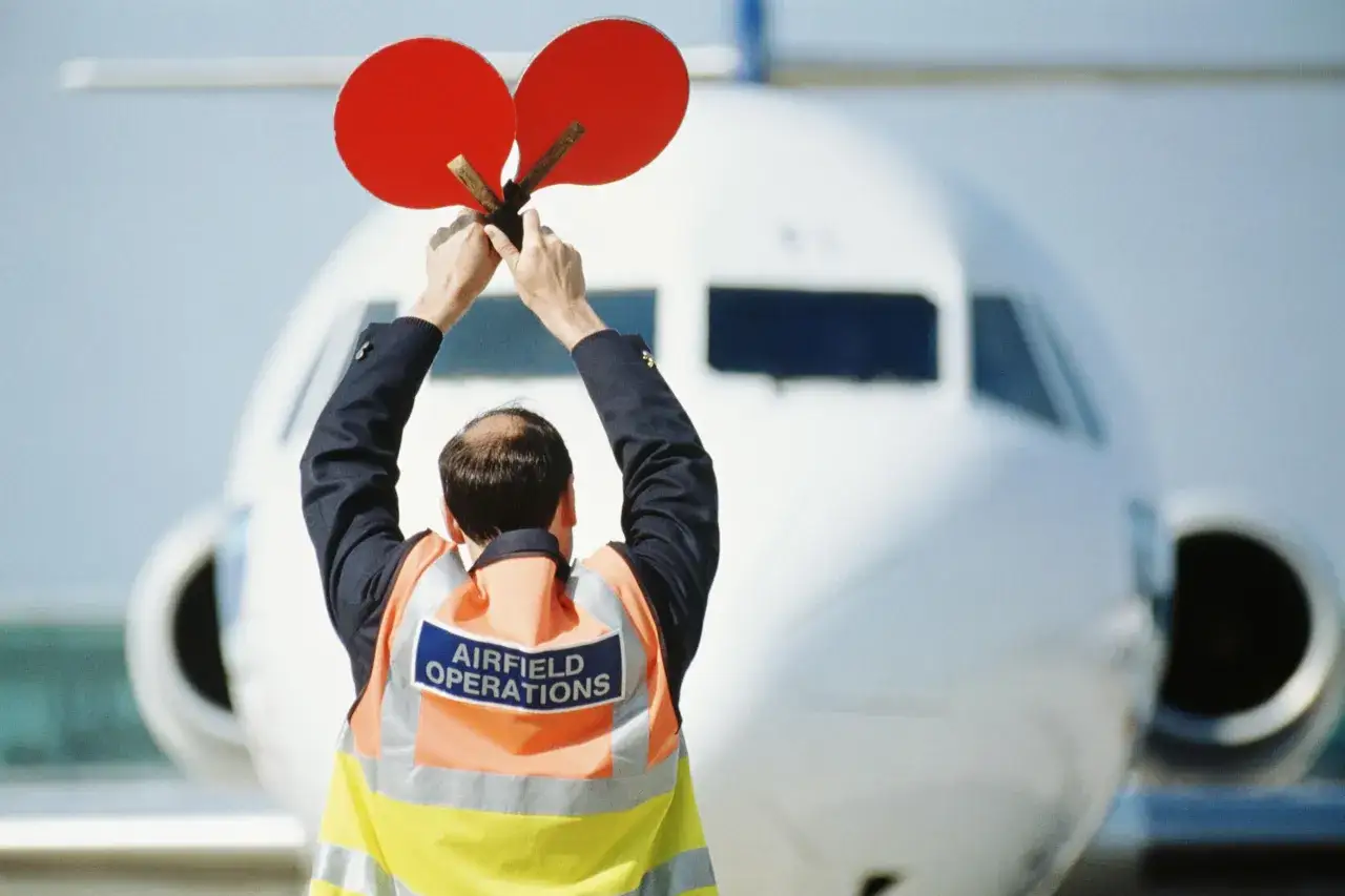 Ein Fluglotse mit roten Scheiben dirigiert ein Flugzeug. Dies ist ein Zeichen für die Sicherheit, die die sicherste Fluggesellschaft der Welt auszeichnet.