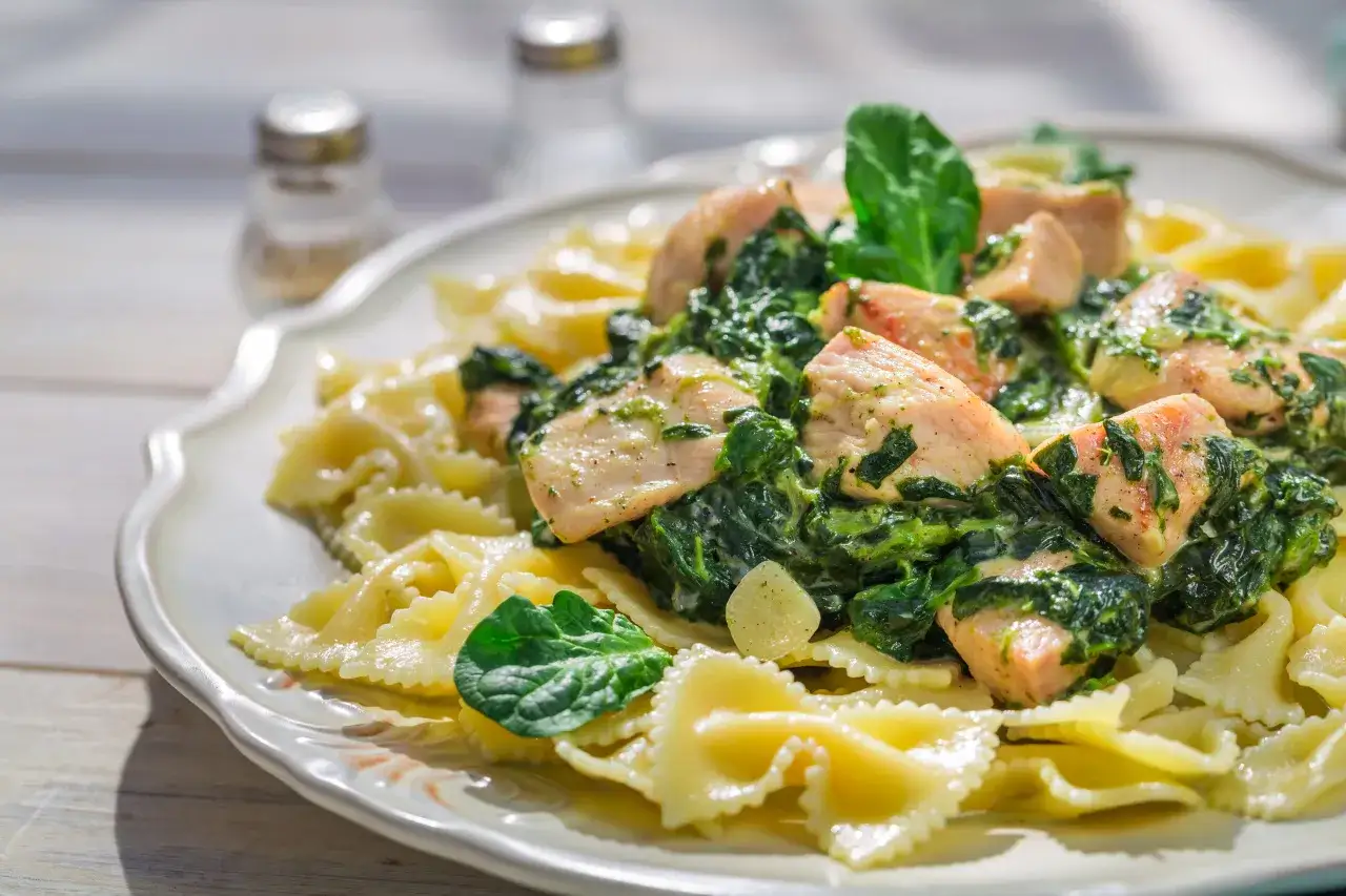 Pyszne potrawy ze szpinakiem świeżym i kurczakiem na makaronie farfalle. Danie wygląda apetycznie i zdrowo.