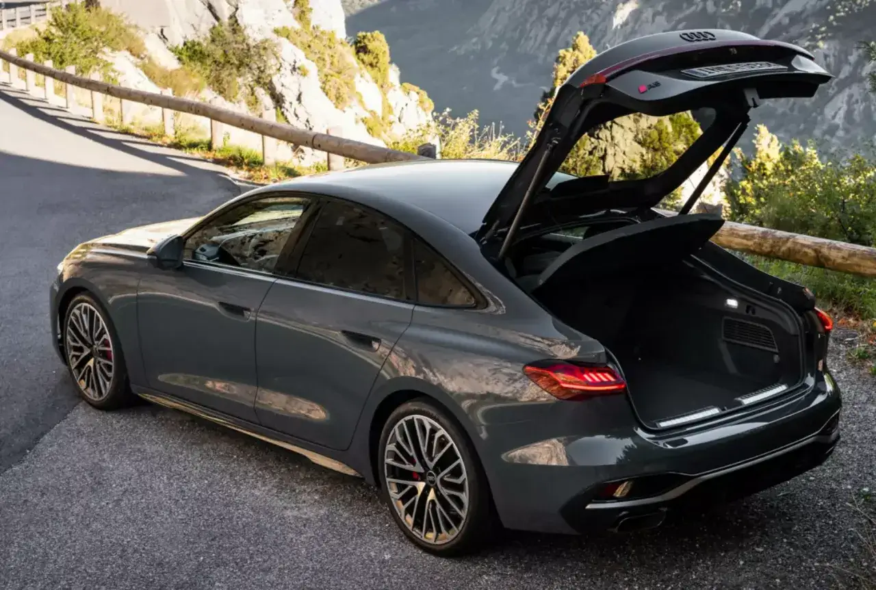 Szary hatchback Audi z otwartym bagażnikiem na górskiej drodze.