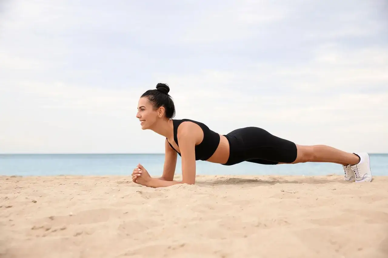 Frau macht Plank-Übung am Strand. Perfektes Training im Urlaub für Körper und Geist.