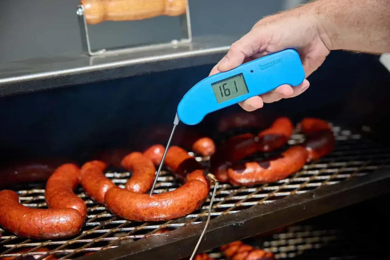Saucisses sur le gril, vérification de la température cuisson saucisse barbecue avec un thermomètre bleu affichant 161.