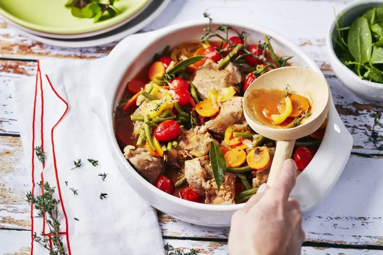Un plat généreux de blanquette de veau, garni de carottes, haricots verts et tomates cerises, prêt à être servi.