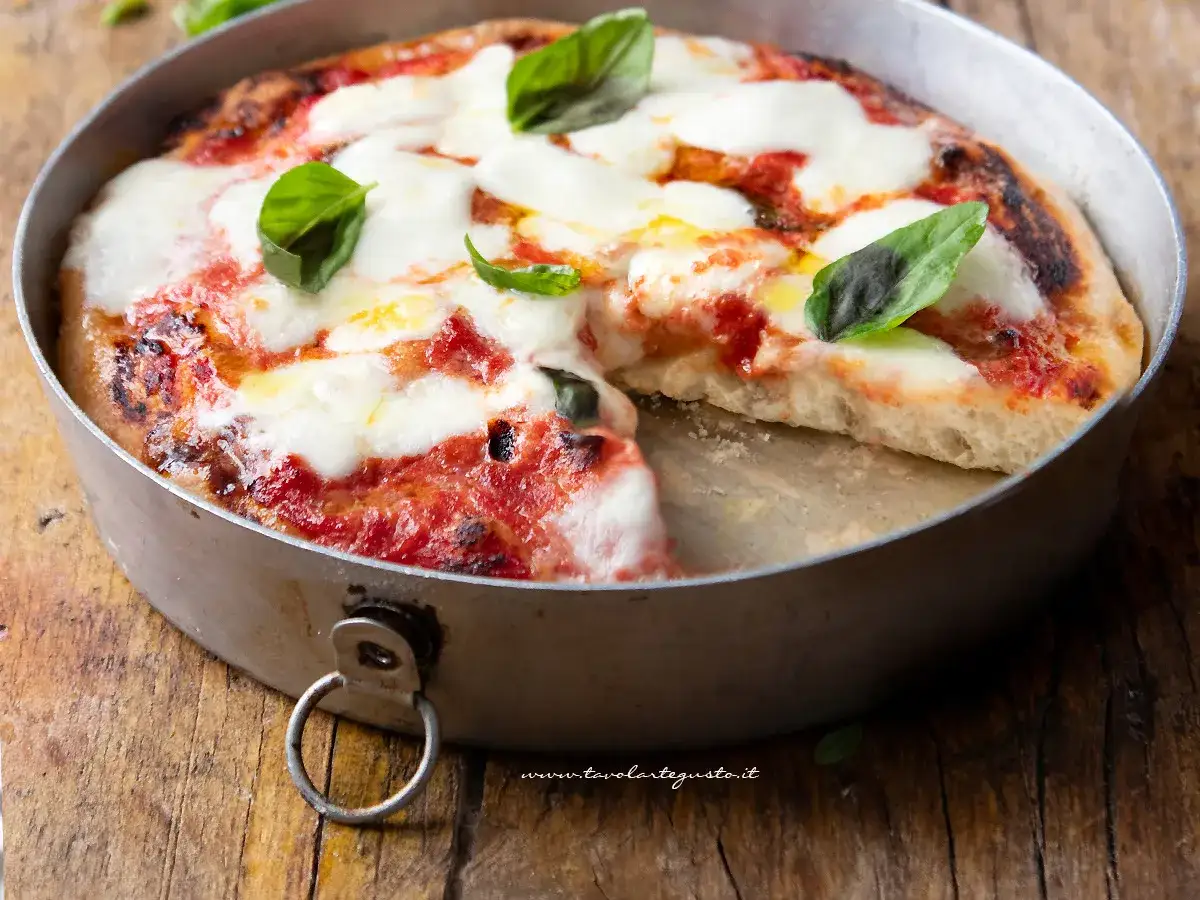Pizza margherita appena sfornata in friggitrice ad aria, con mozzarella filante e basilico fresco su un tagliere di legno.