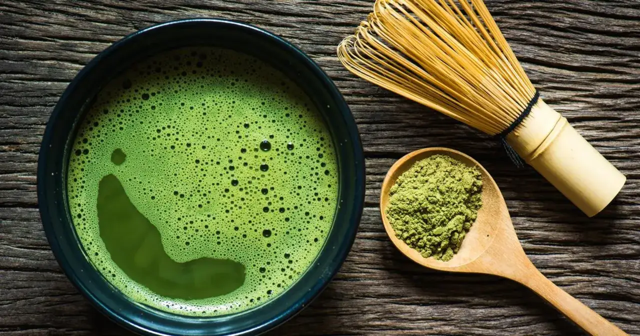 Puszysta zielona matcha w miseczce, obok bambusowa miotełka i łyżka z proszkiem. Idealna matcha jaką wybrać na początek.