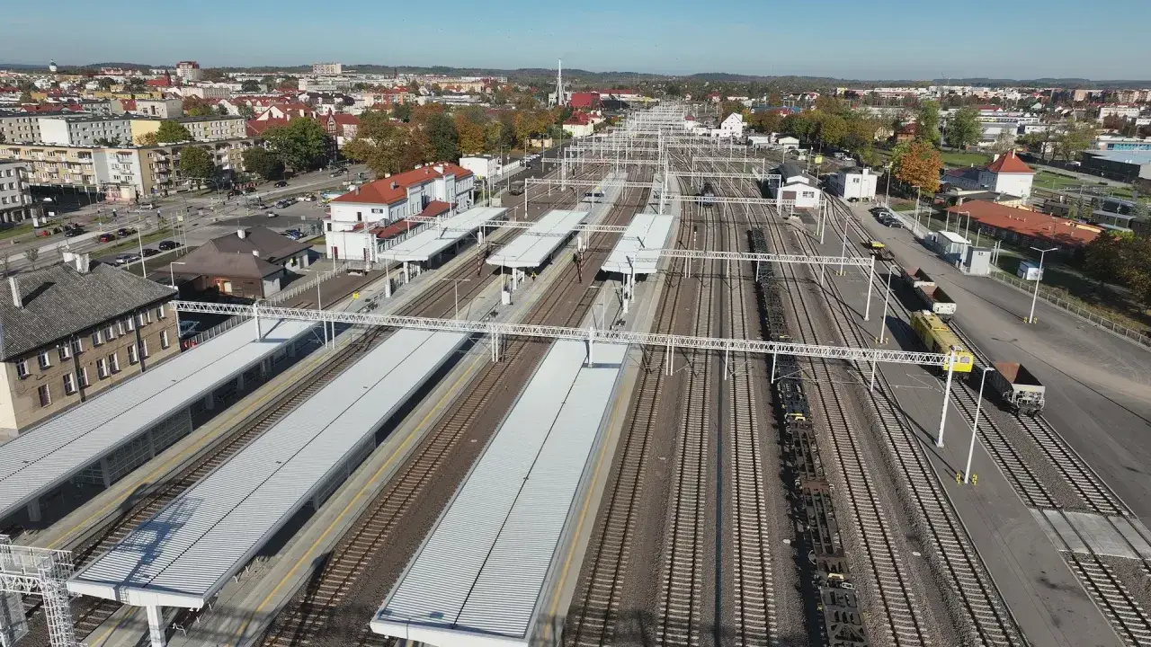 Widok z lotu ptaka na dworzec PKP Ełk z licznymi torami, peronami i budynkami. W oddali widać miasto.