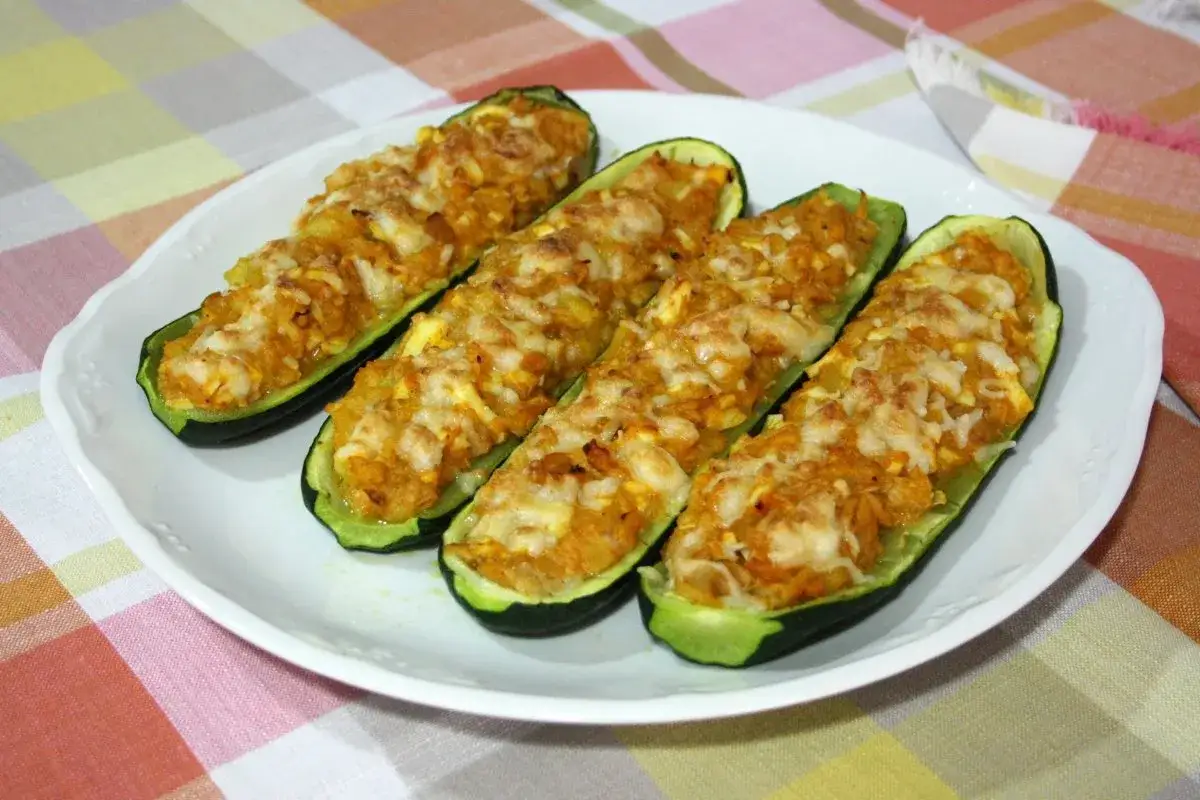 Cuatro calabacines rellenos, gratinados con queso, servidos en un plato blanco sobre un mantel a cuadros.