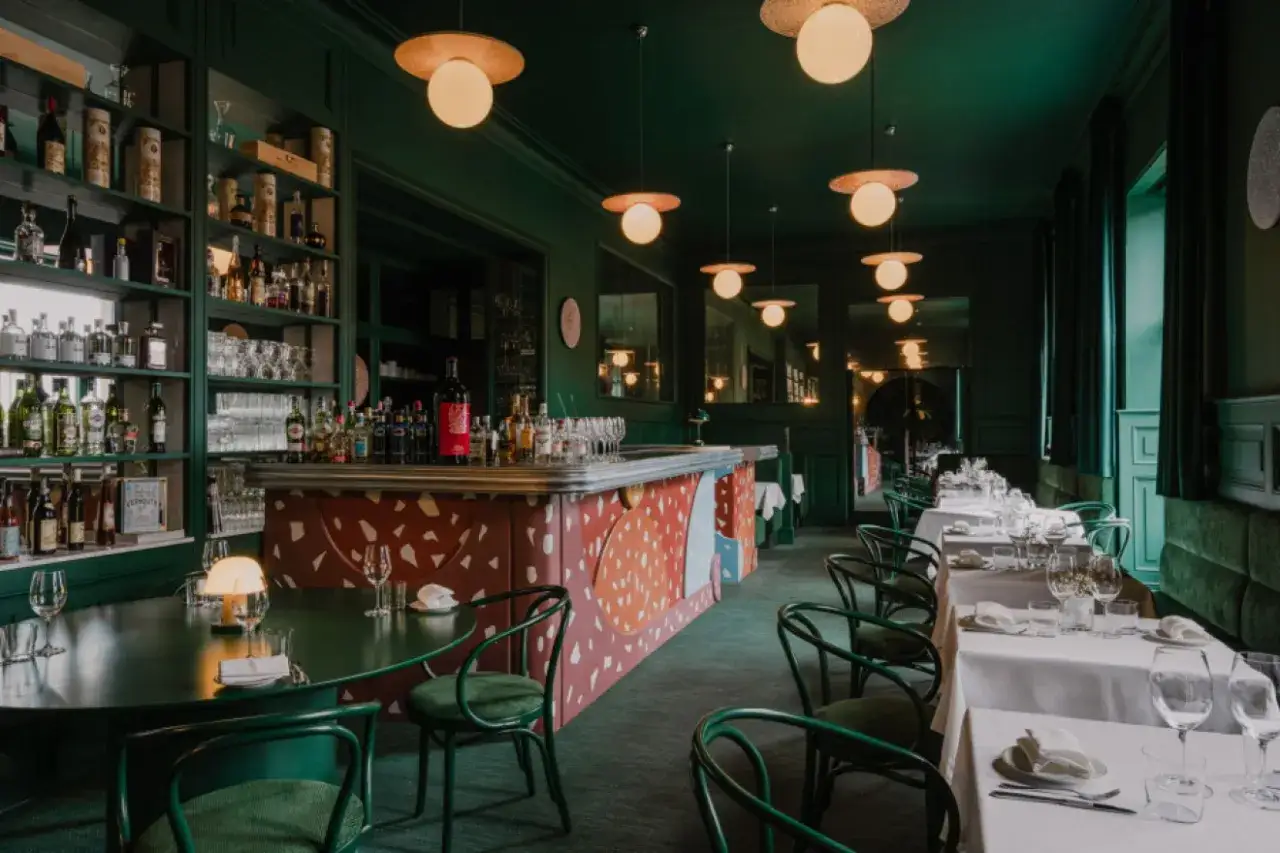 Elegancka restauracja z zielonym wystrojem, barem i stolikami nakrytymi do kolacji. Miejsce godne gwiazdki Michelin w Polsce.